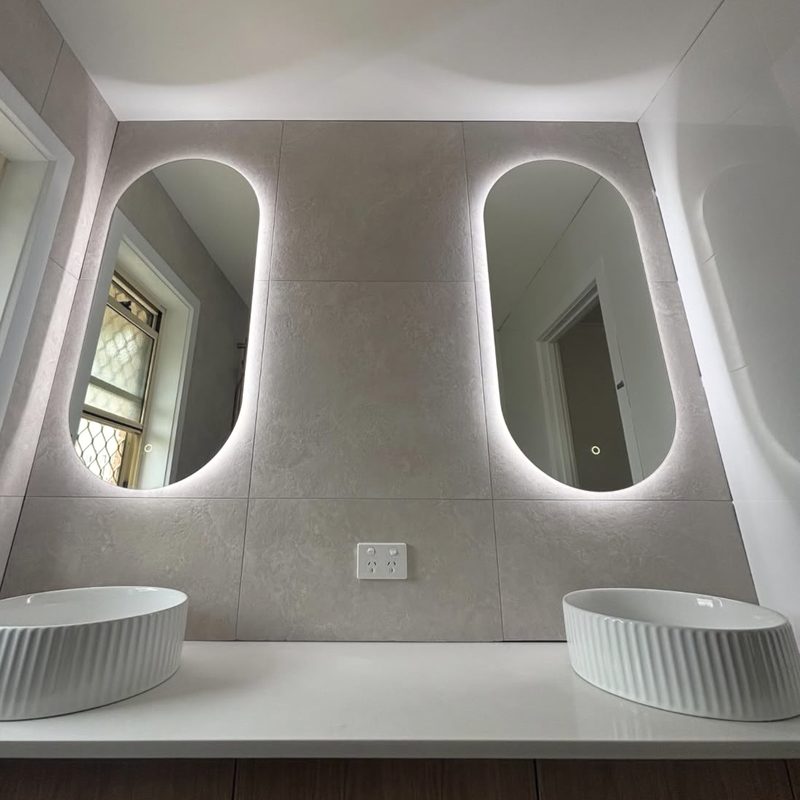 Backlit LED mirrors over a double vanity in a renovated bathroom